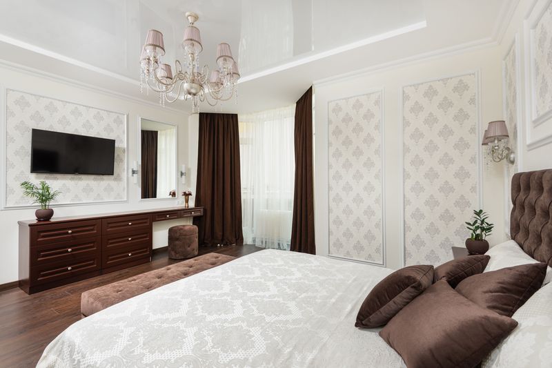 Classic bedroom suite with ivory damask wallpaper set into moulded wall panels, a chandelier and chocolate-brown accents