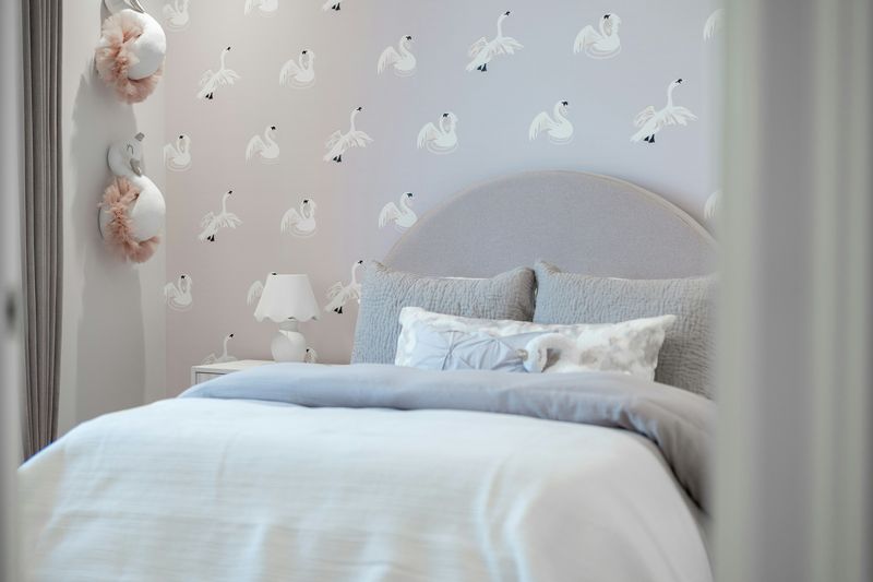 Soft grey bedroom with swan-motif wallpaper behind an arched upholstered headboard and pale blue bedding