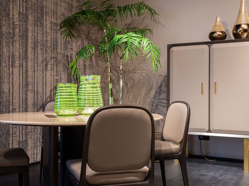 Dining area with a weathered, vertical-texture mural wallcovering, a round stone table, leather chairs and green glass vases