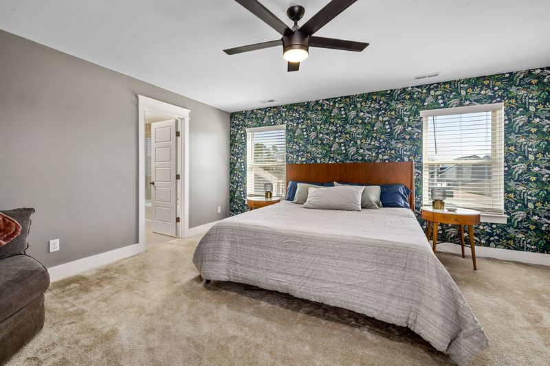 Spacious bedroom with a dark botanical-print wallpaper accent wall framing two windows behind a wooden bed