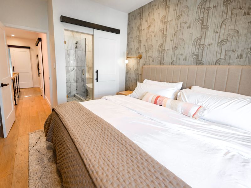 Modern bedroom with an abstract arched-stroke wallcovering in grey and taupe behind a channel-tufted headboard